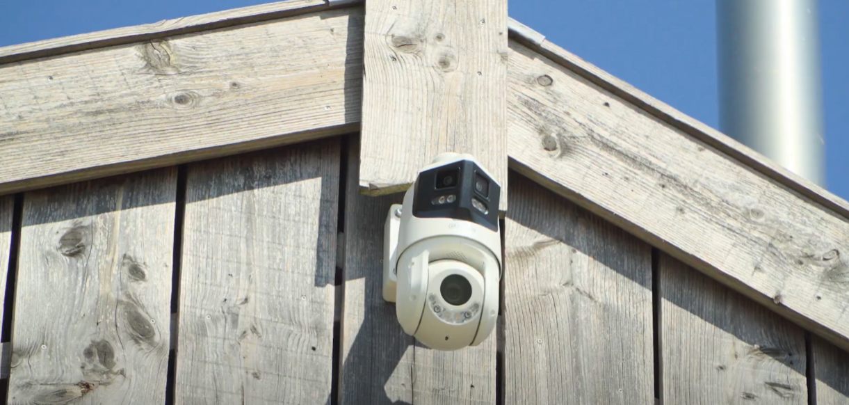Witte beveiligingscamera gemonteerd op een houten gevel.