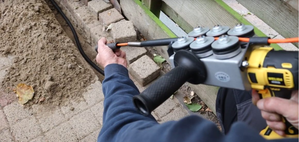 Monteur boort een doorvoer voor de kabelroute in de tuin van een woning.