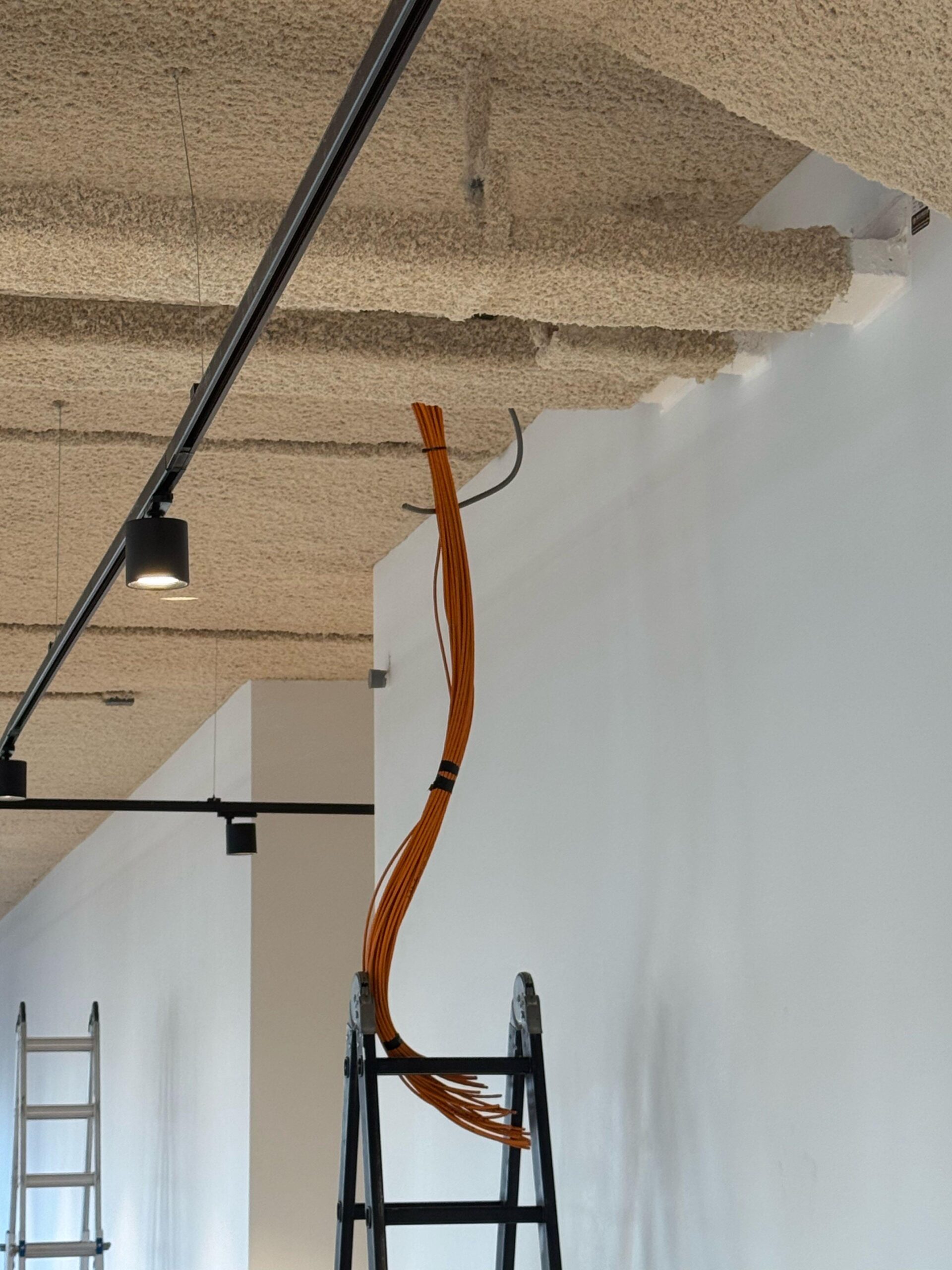 Een bundel oranje UTP-netwerkkabels wordt vanaf een ladder door het plafond van een bedrijfspand getrokken.