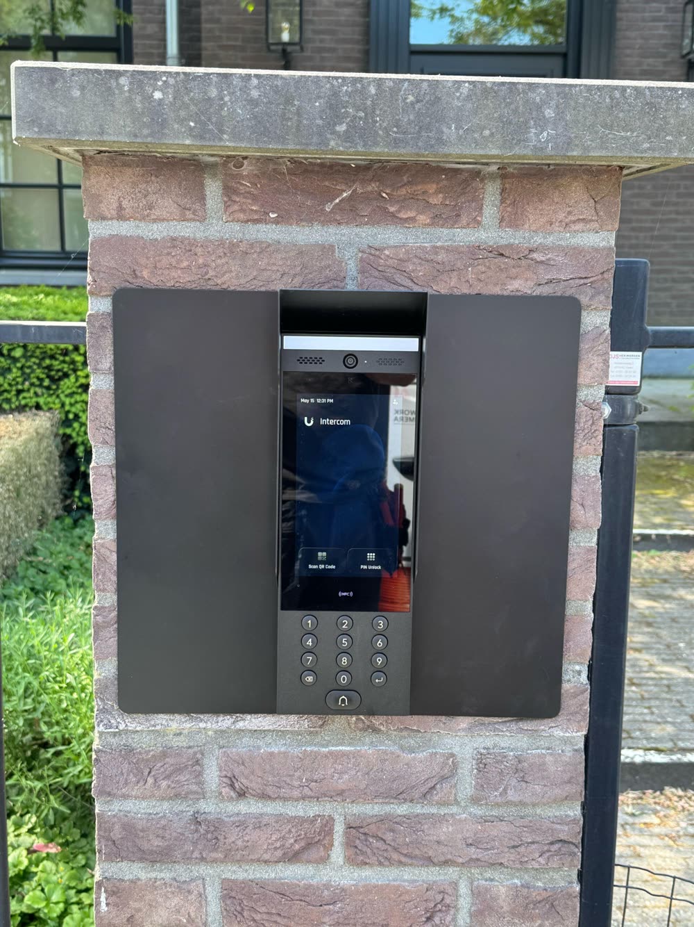 Deurstation met camera, touchscreen en keypad in een bakstenen gevelzuil.