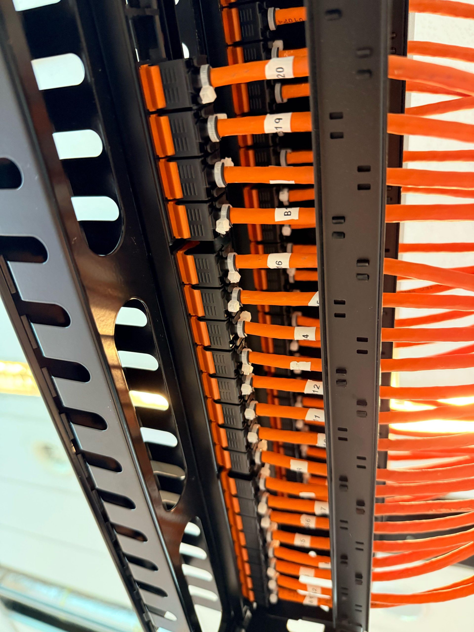 Oranje netwerkkabels, genummerd met de labels 12, 16, 19 en 20, in de kabelgeleiding van een rack.