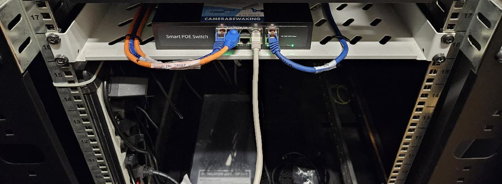 PoE-switch in een 19-inch serverrek met gelabelde oranje en blauwe patchkabels.