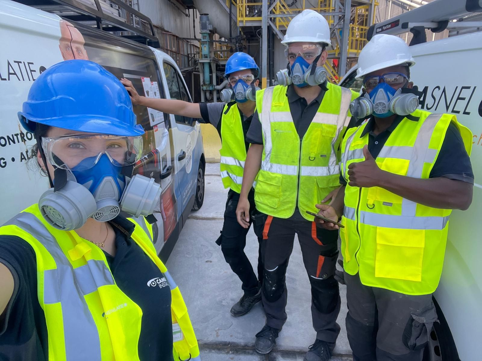 Installatieteam met helmen en ademhalingsmaskers op een industriële locatie.