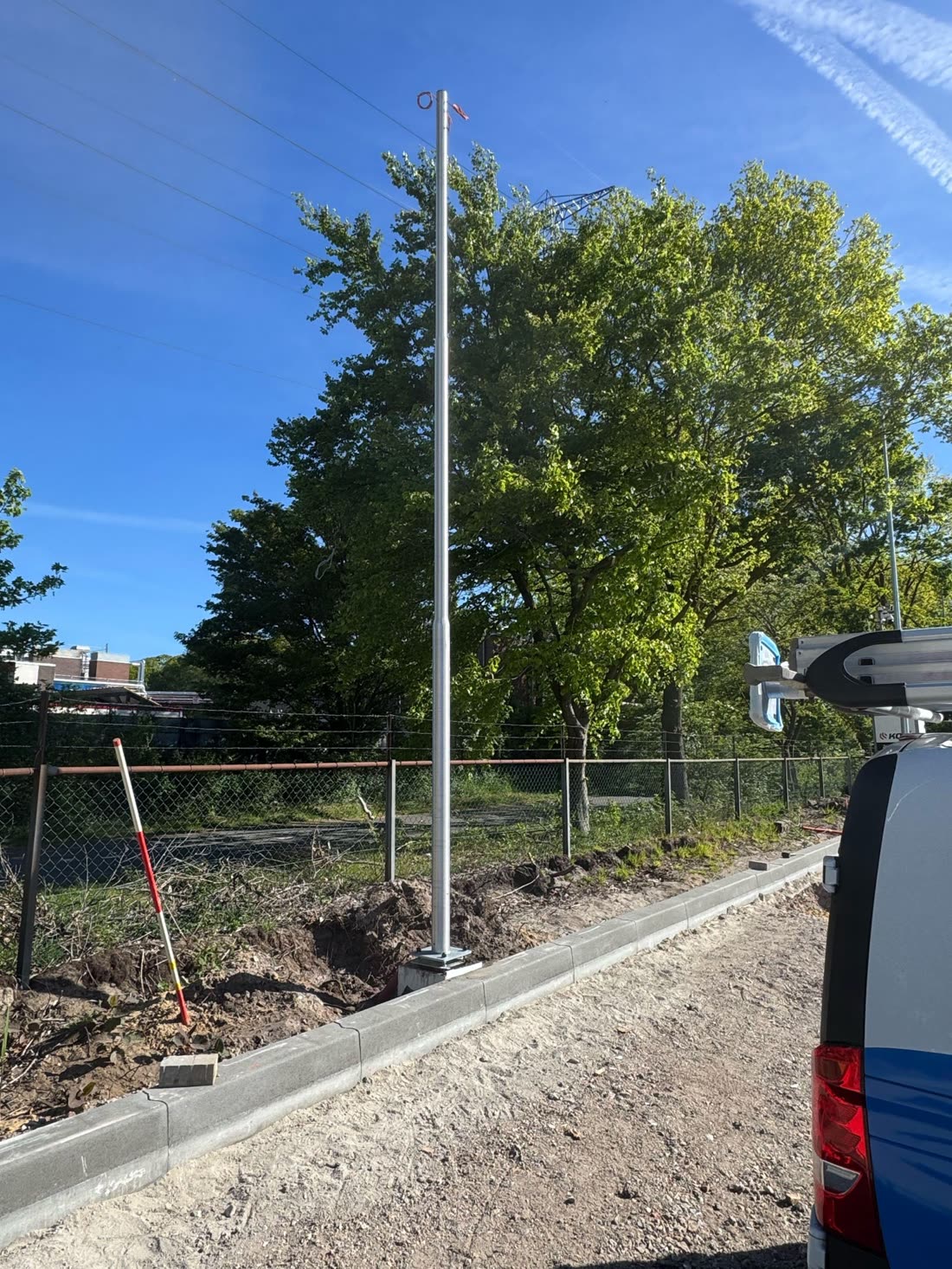 Kabelsleuf langs een bedrijfsterrein met een nieuw geplaatste mast en een servicebus ernaast.