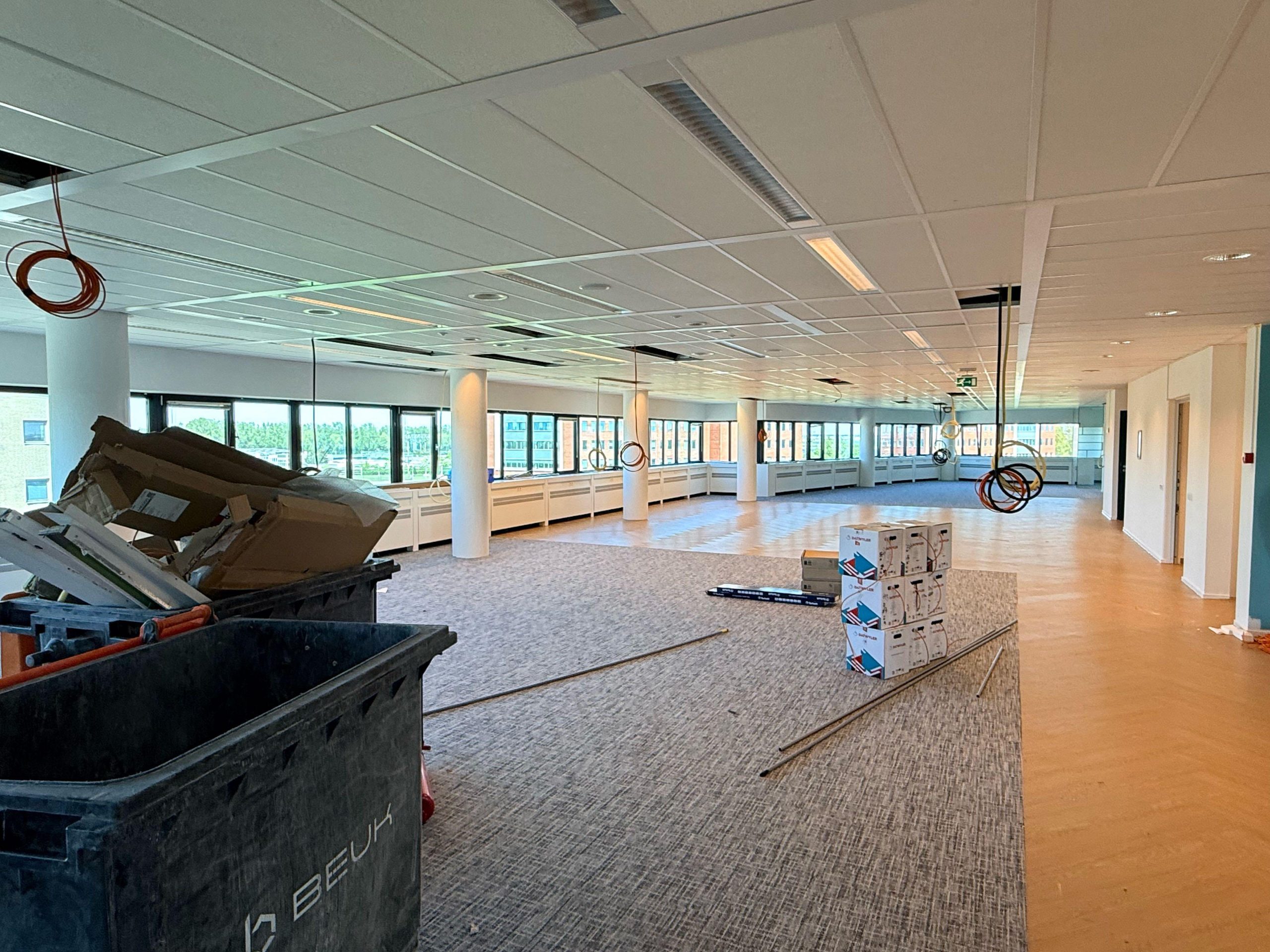 Ruime kantoorvloer in aanbouw, met kabelrollen aan het plafond en stapels dozen netwerkkabel op de vloer.