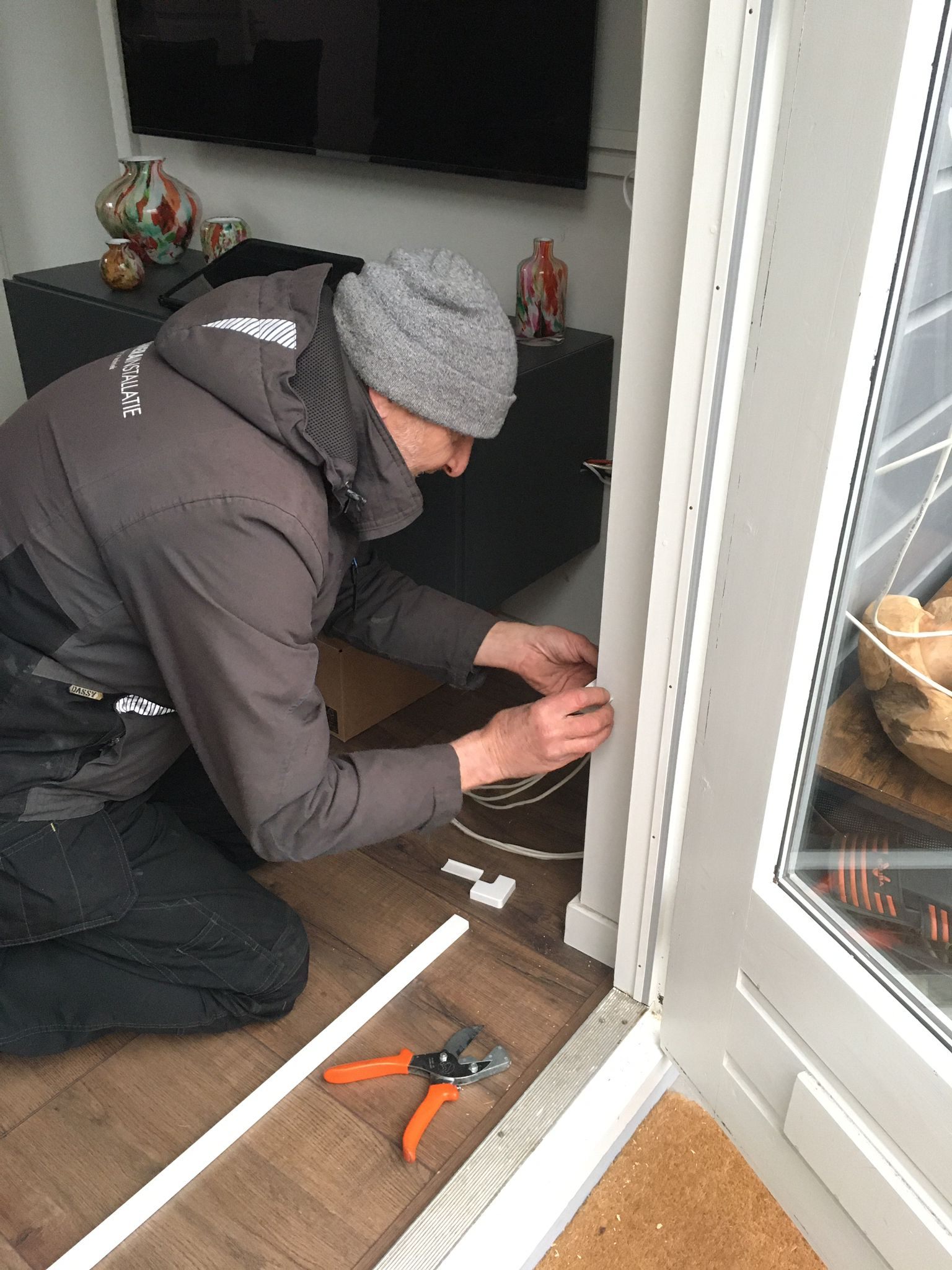 Monteur legt bekabeling langs een raamkozijn.