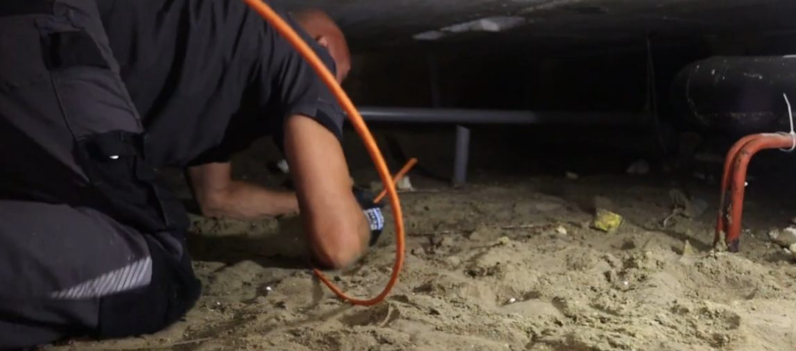 Monteur trekt een kabel door de kruipruimte van een woning.