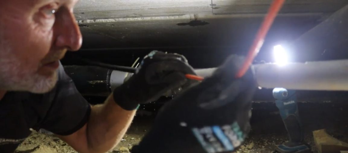 Monteur trekt liggend een kabel verder door de kruipruimte.