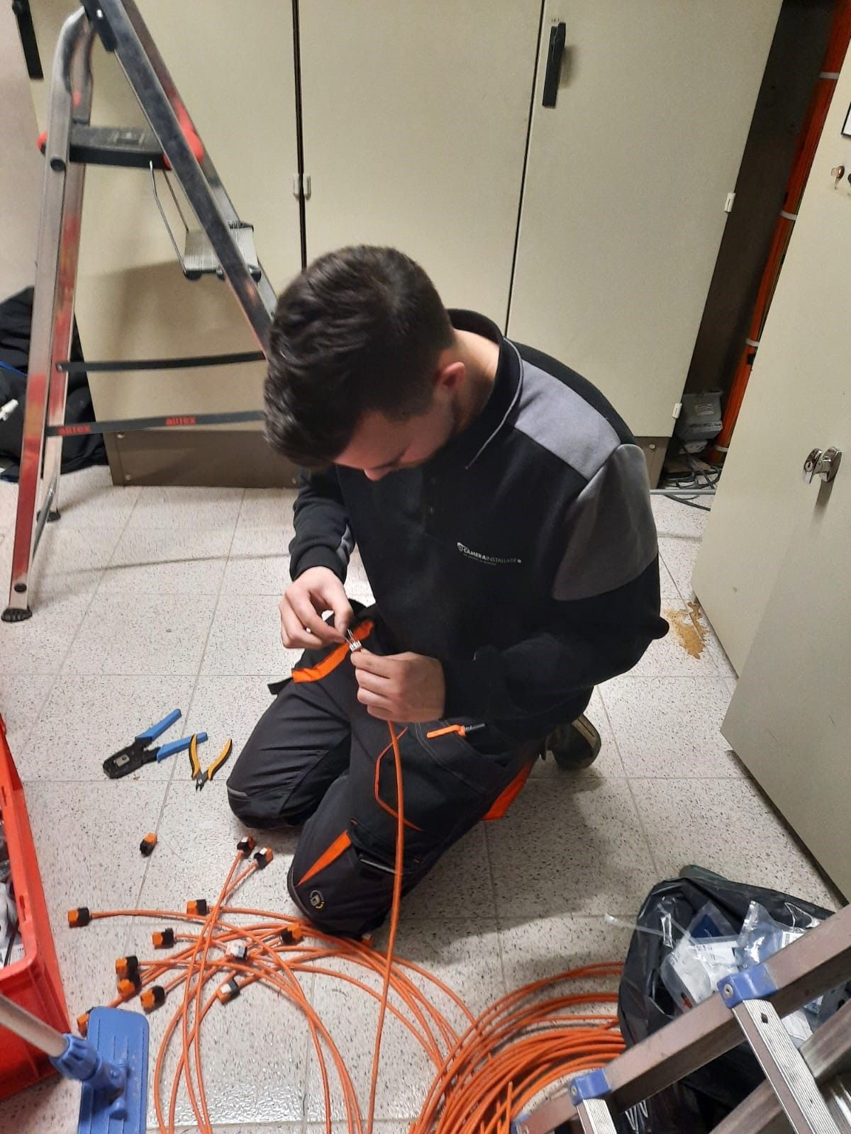 Monteur werkt aan oranje netwerkkabels in een technische ruimte.