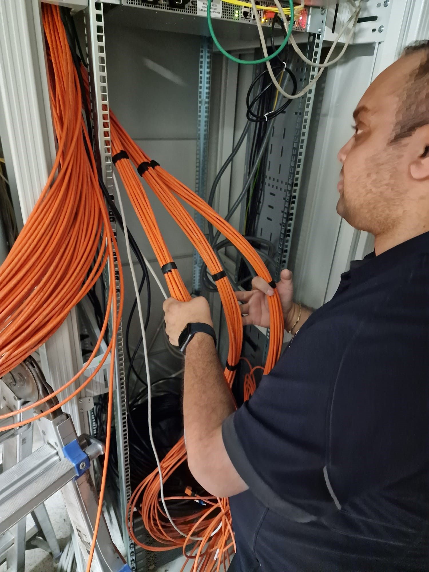 Monteur werkt aan een patchkast met patchpanelen en netwerkkabels.