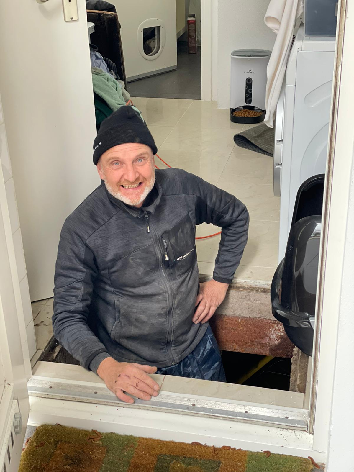Monteur werkt in de kruipruimte onder een woning aan de bekabeling.