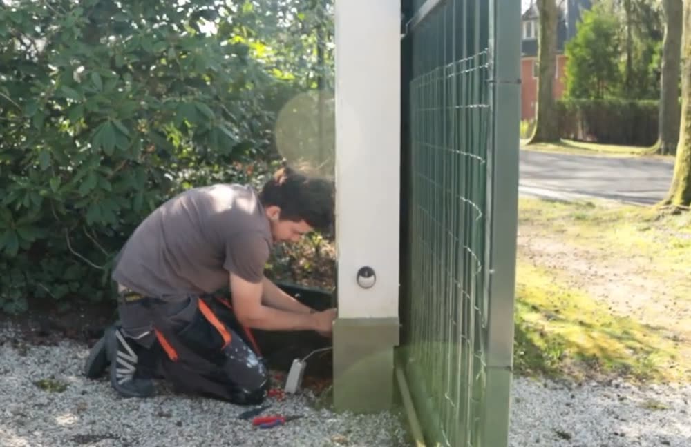 Twee monteurs plaatsen een intercomzuil bij de inrit van een terrein.