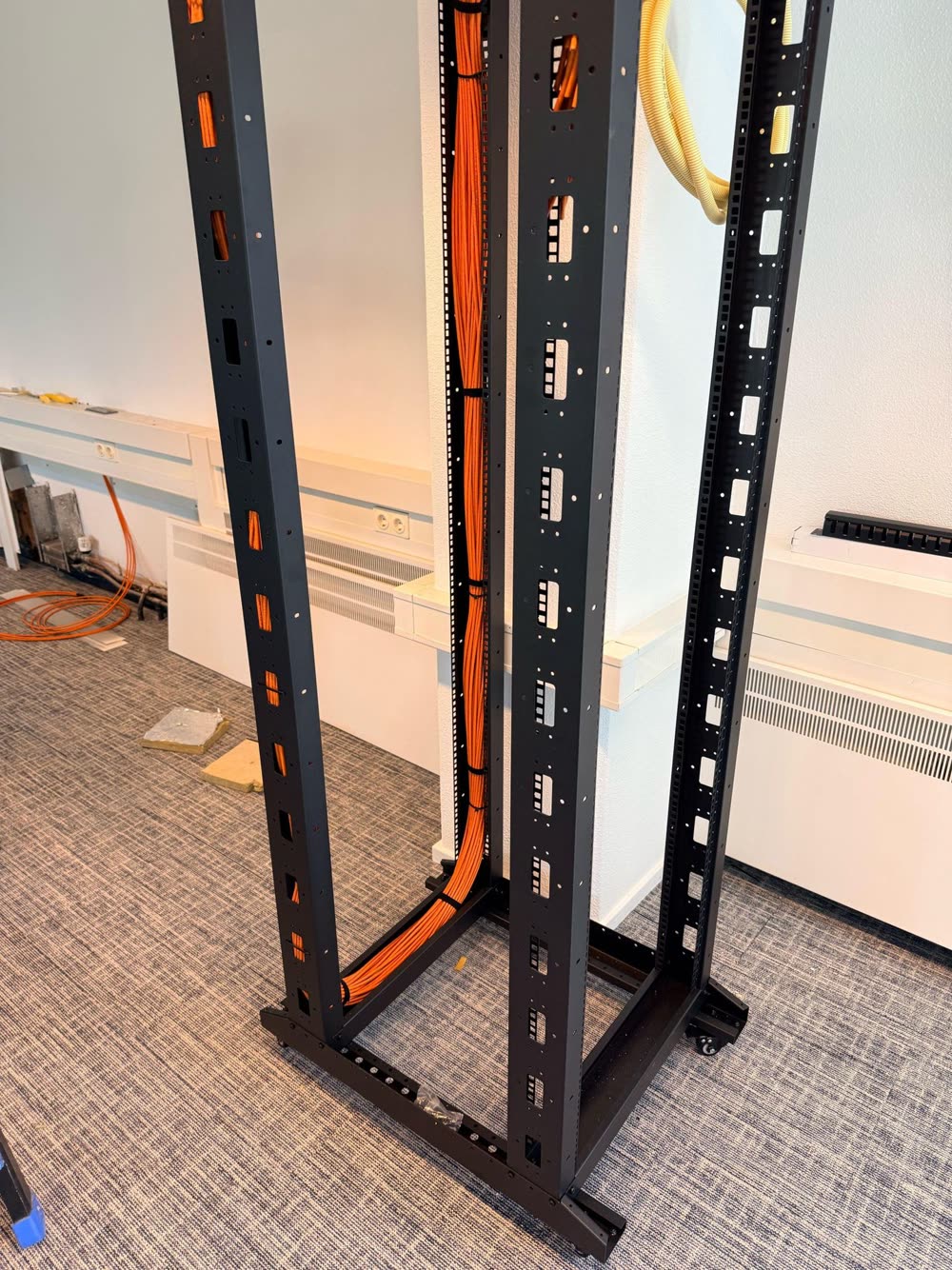 Open 19-inch rack met oranje datakabels die van boven worden ingevoerd.