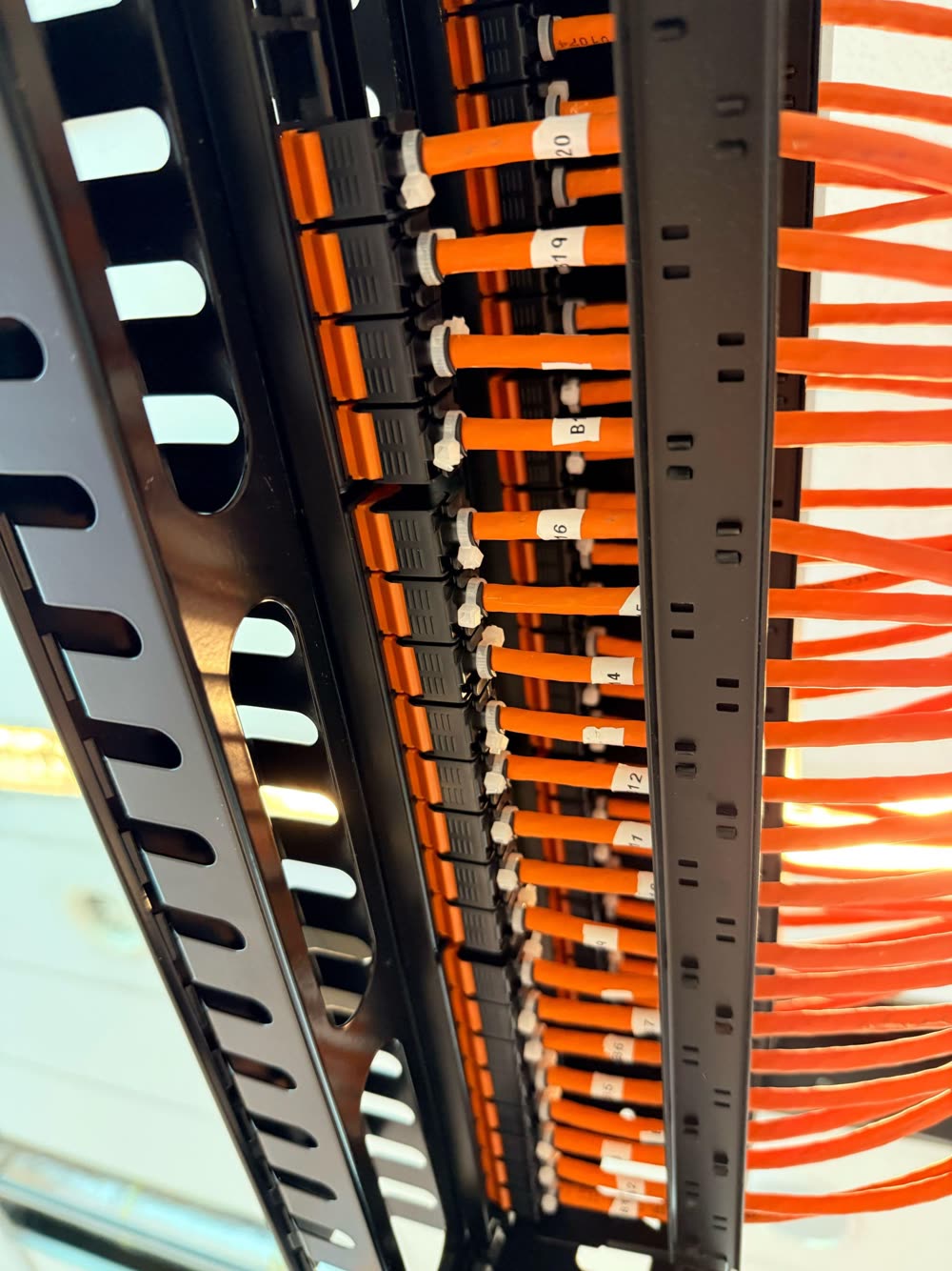 Oranje datakabels netjes geleid door de kabelgeleiding van een rack.