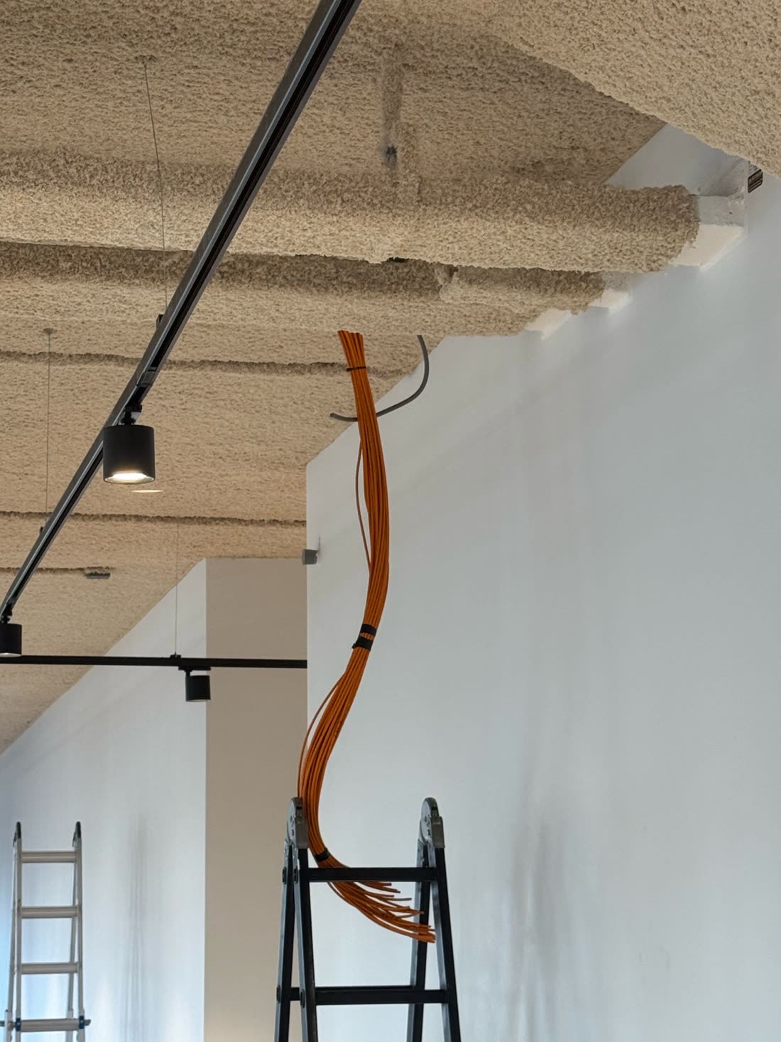 Bundel oranje datakabels langs het plafond tijdens de aanleg, met ladders eronder.