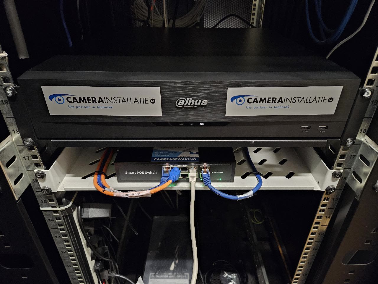 Netwerkvideorecorder en PoE-switch in een 19-inch serverrek, met gelabelde oranje en blauwe patchkabels.