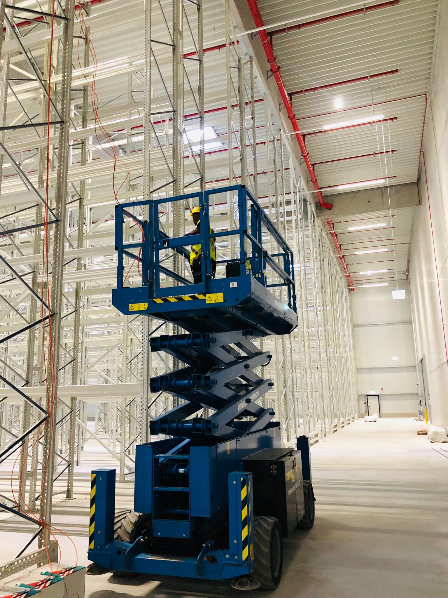 Schaarhoogwerker in een industriële hal tijdens installatiewerk op hoogte.