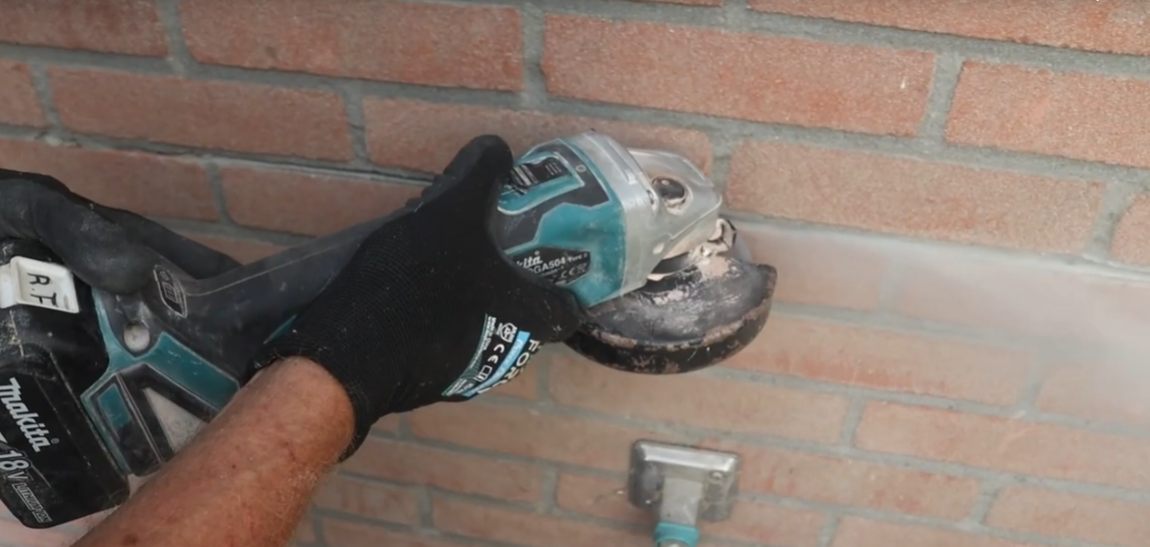 Sleuf slijpen in de voeg van een bakstenen muur voor een kabelroute.