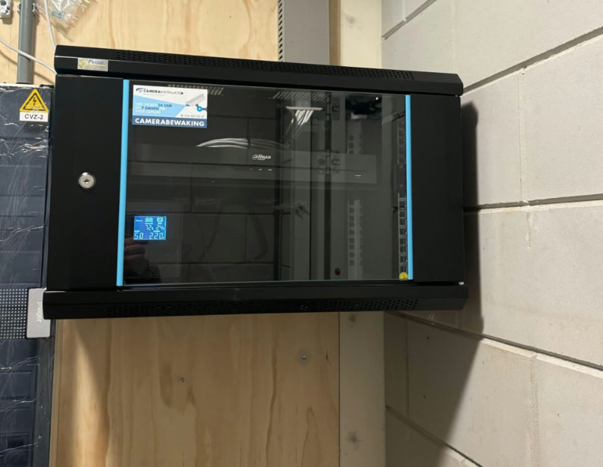 Wandpatchkast met glazen deur en UPS-display in een technische ruimte, gemonteerd op multiplex.