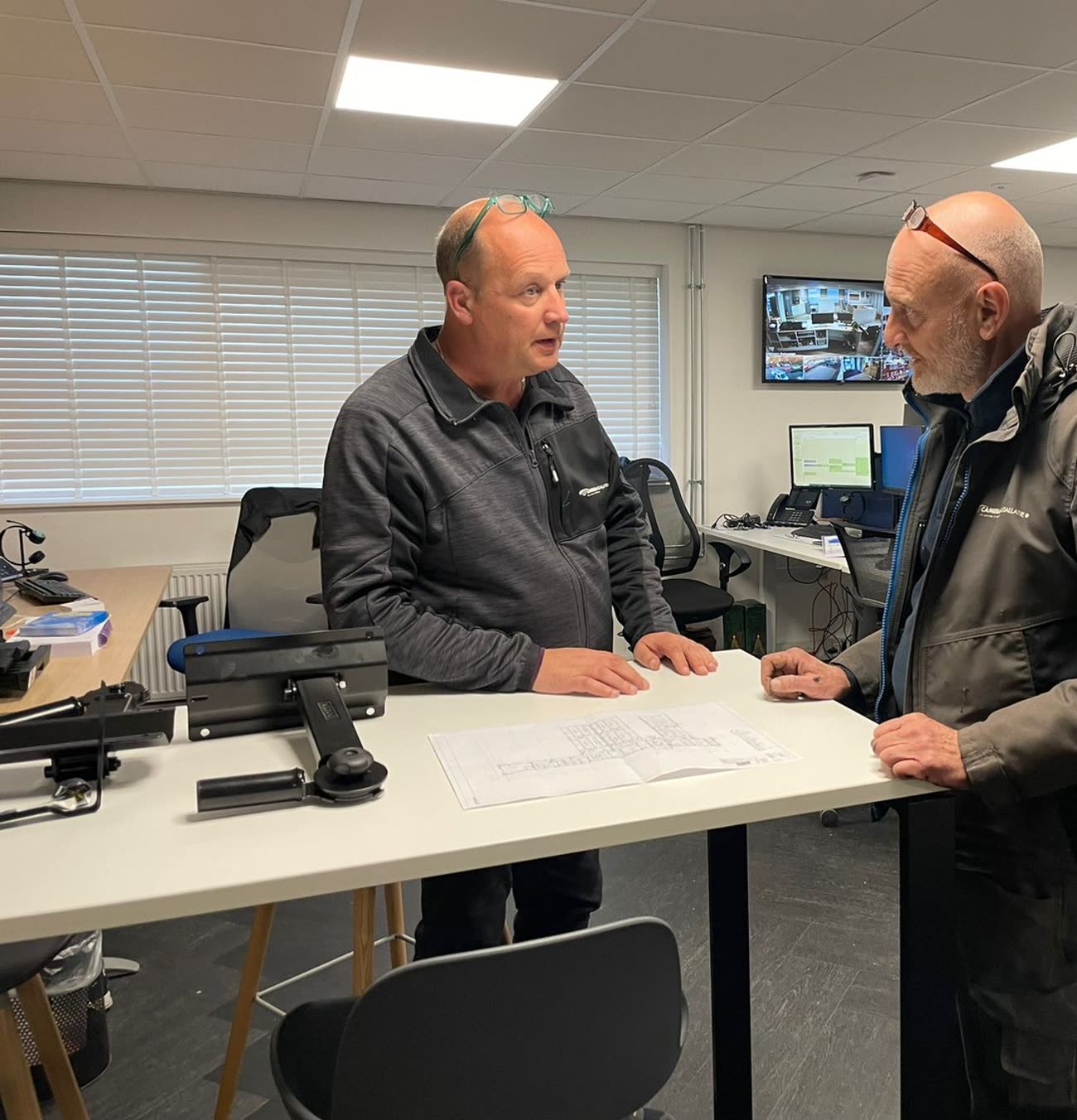 Twee collega's bespreken staand een installatietekening op kantoor.