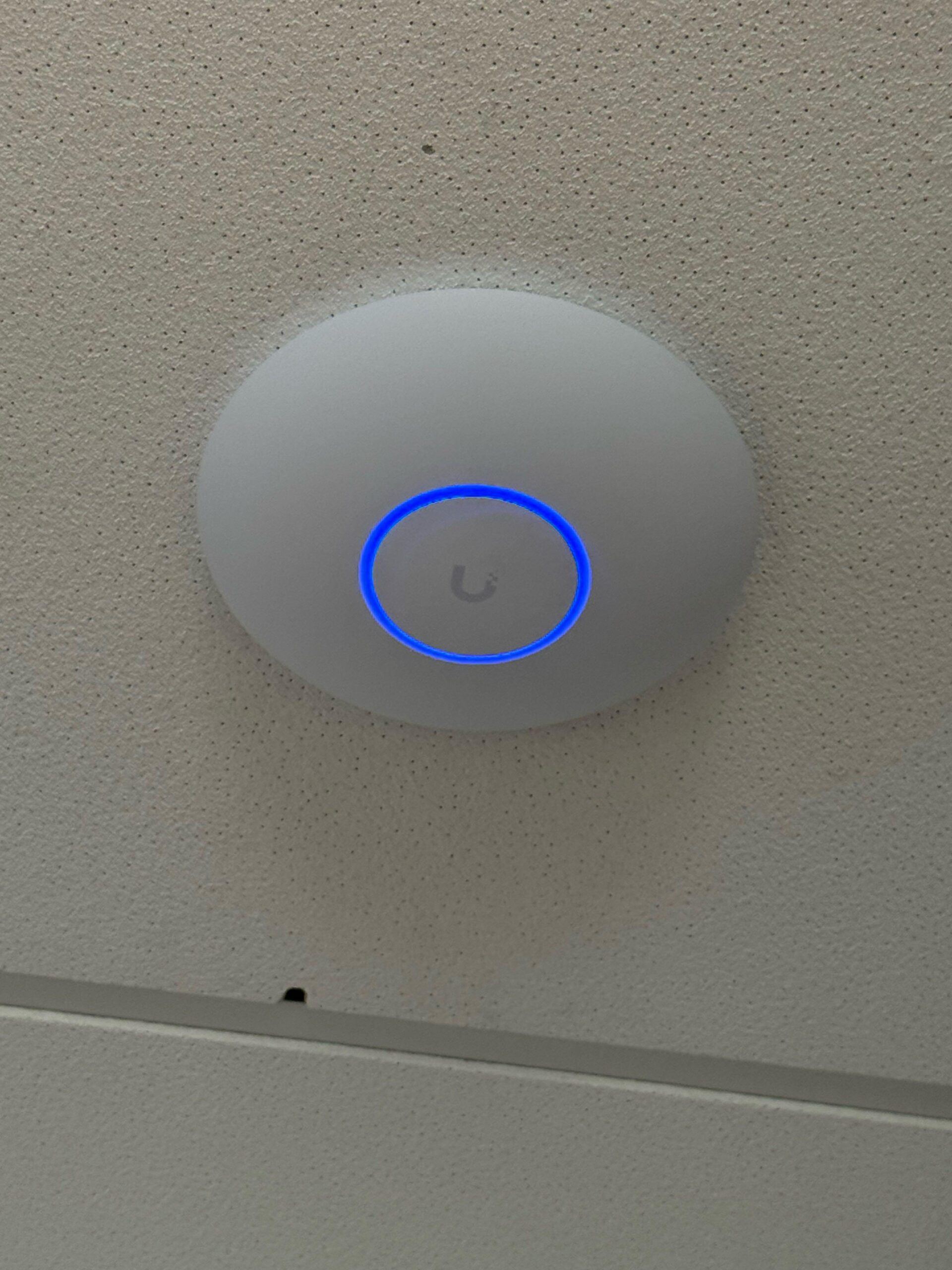 Wit plafond-accesspoint met blauwe lichtring, strak gemonteerd in een systeemplafond.