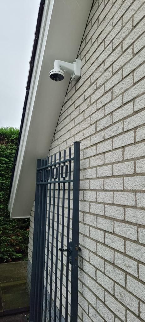 Witte beveiligingscamera aan de zijgevel van een woning.