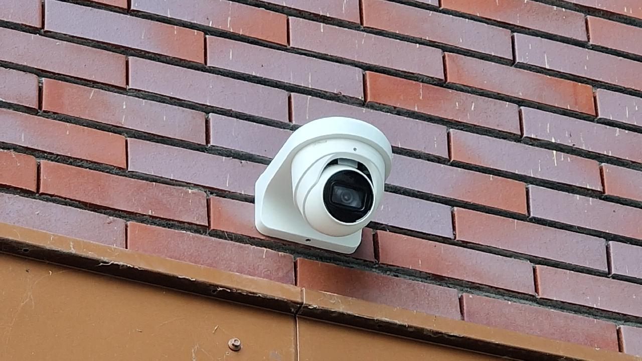 Witte domecamera aan de bakstenen gevel van een schoolgebouw.