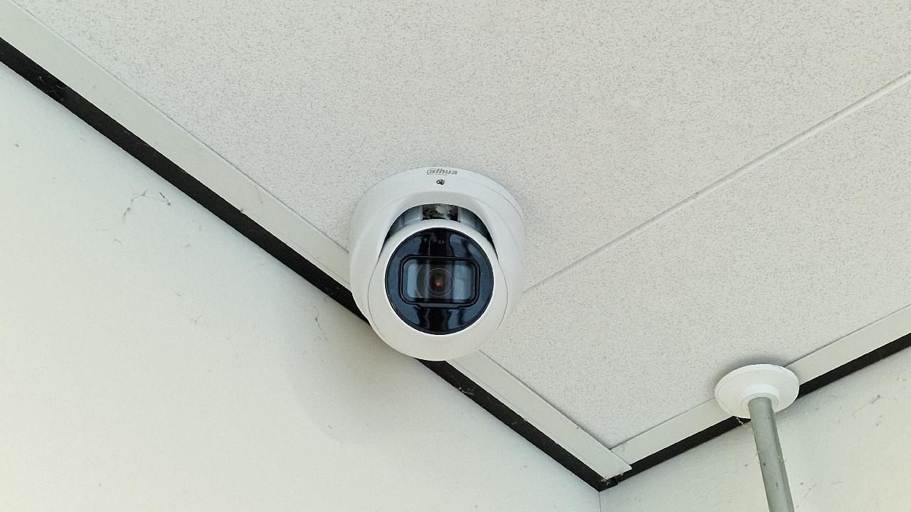 Witte domecamera aan het plafond van een gang in een schoolgebouw.