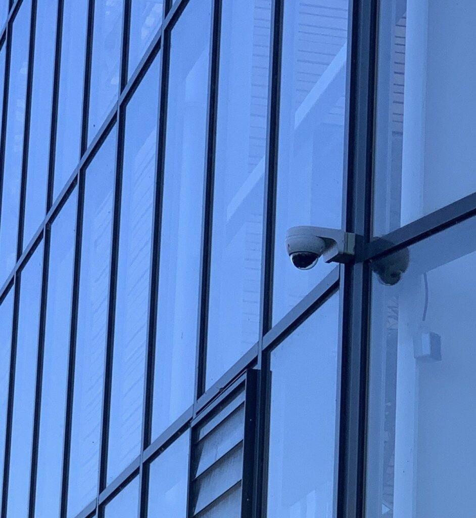 Camera op een beugel aan de glazen gevel van een campusgebouw.