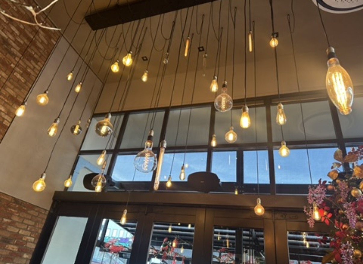 Tientallen hanglampen met filamentlampen op verschillende hoogtes voor een hoge glazen pui.