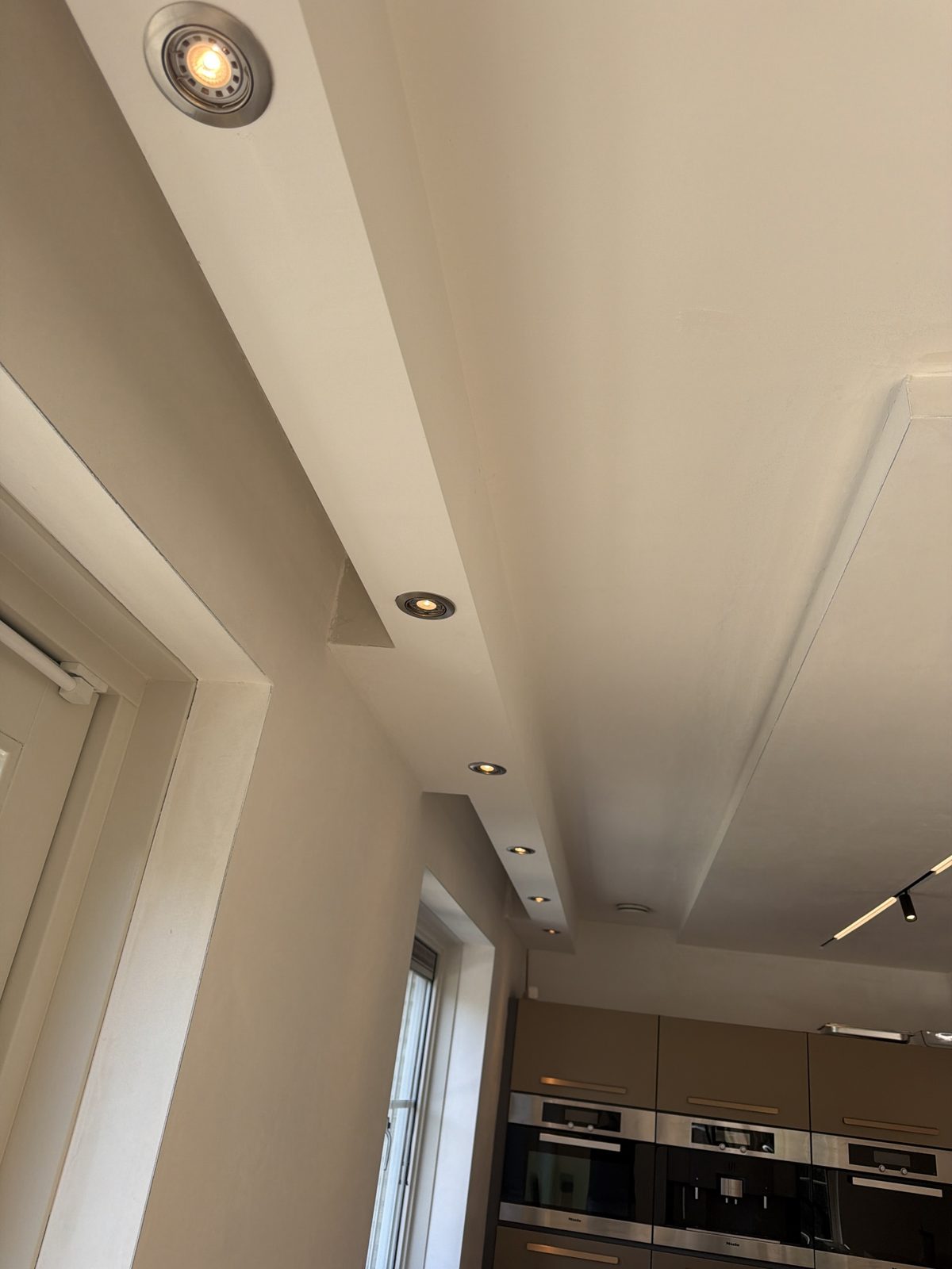 Rij inbouwspots in een plafondkoof langs de wand, richting de keuken.