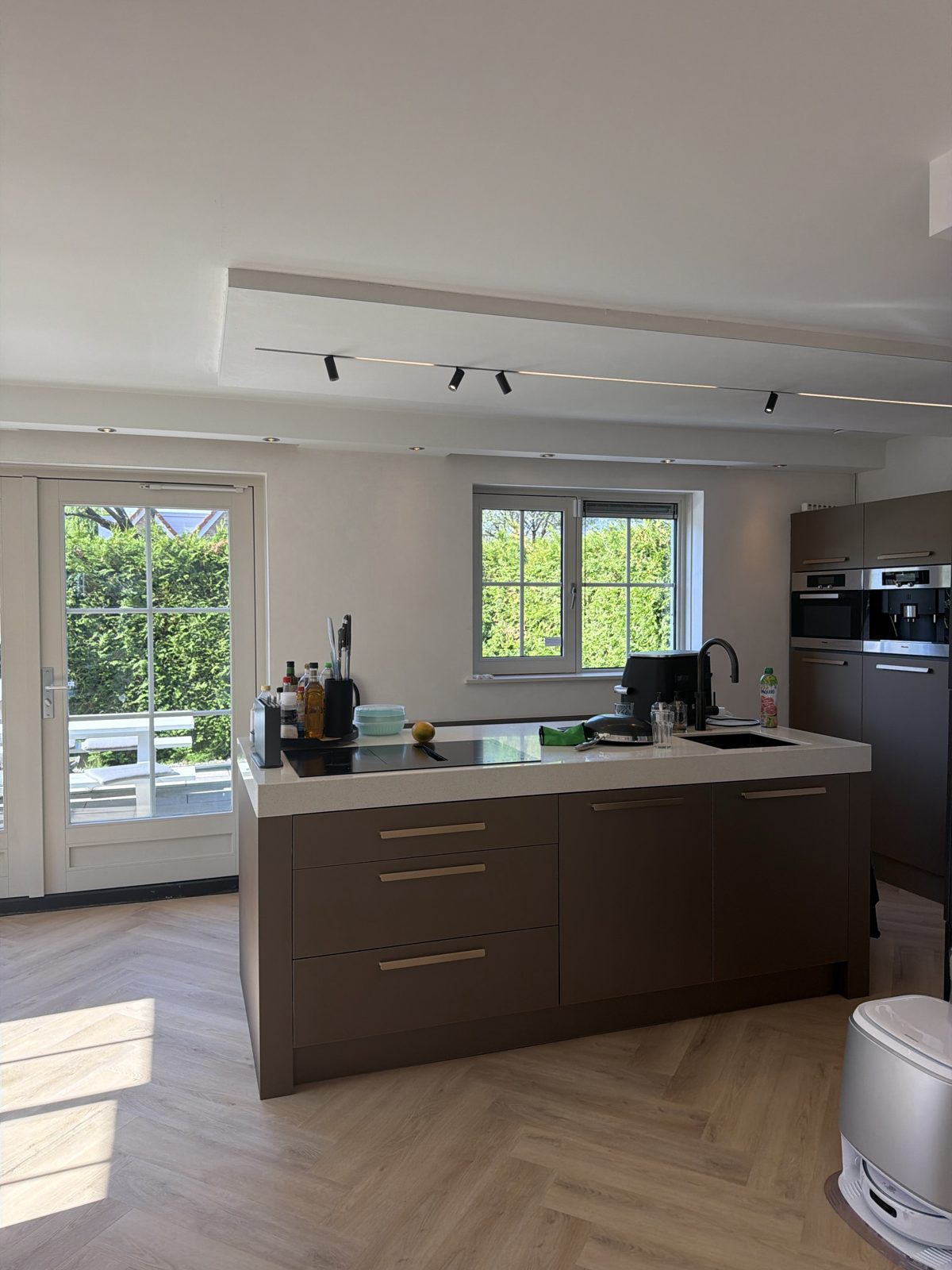 Keuken met kookeiland en inbouwrailverlichting met spots en lichtlijnen in het verlaagde plafond.