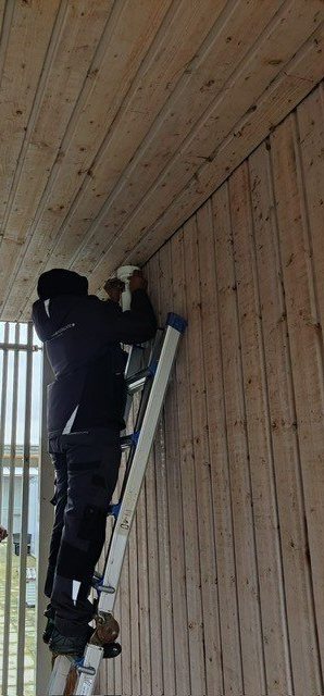 Monteur op een ladder monteert een camera onder een houten overkapping.
