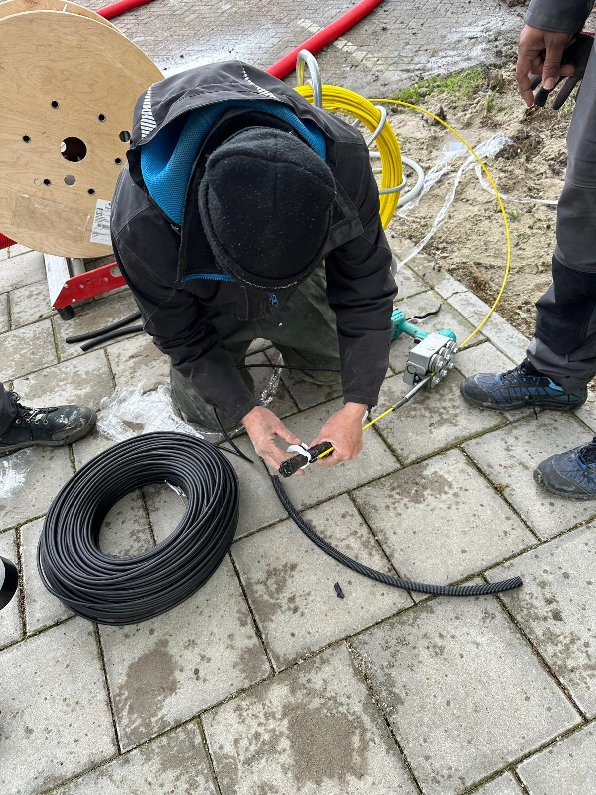 Monteur werkt buiten aan een kabel naast een kabelhaspel.