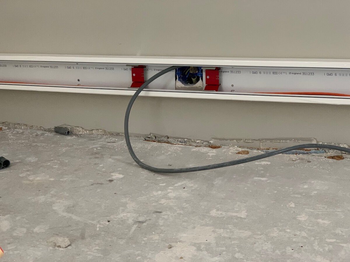 Open kabelgoot met een kabel erin, boven een nog kale betonvloer.