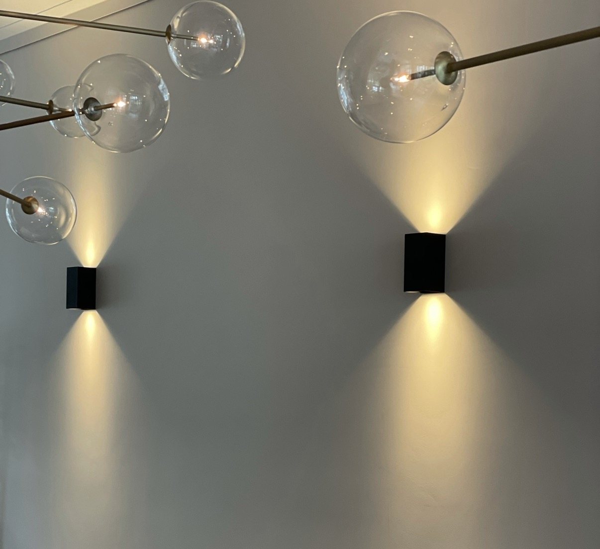 Twee zwarte wandlampen met licht op en neer, onder een designhanglamp met glazen bollen.