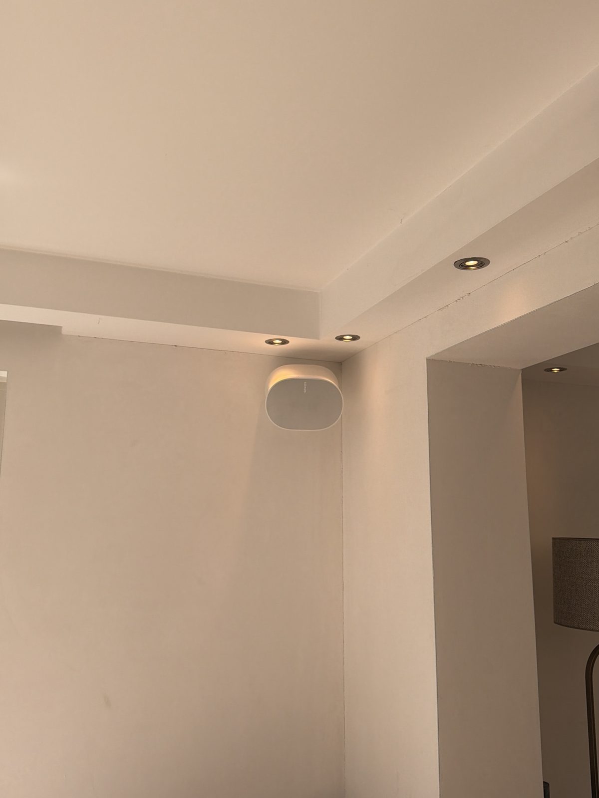 Wandspeaker hoog in de hoek van een woonkamer, met inbouwspots in de plafondrand.