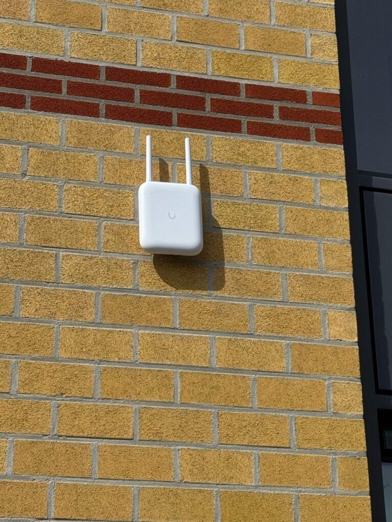 Wifi-zender met twee antennes op een bakstenen buitengevel, voor bereik in de tuin.
