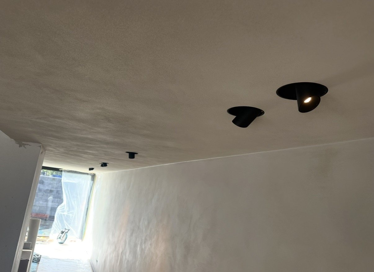 Zwarte kantelbare inbouwspots in een gestuct plafond, tijdens de afbouw van de ruimte.