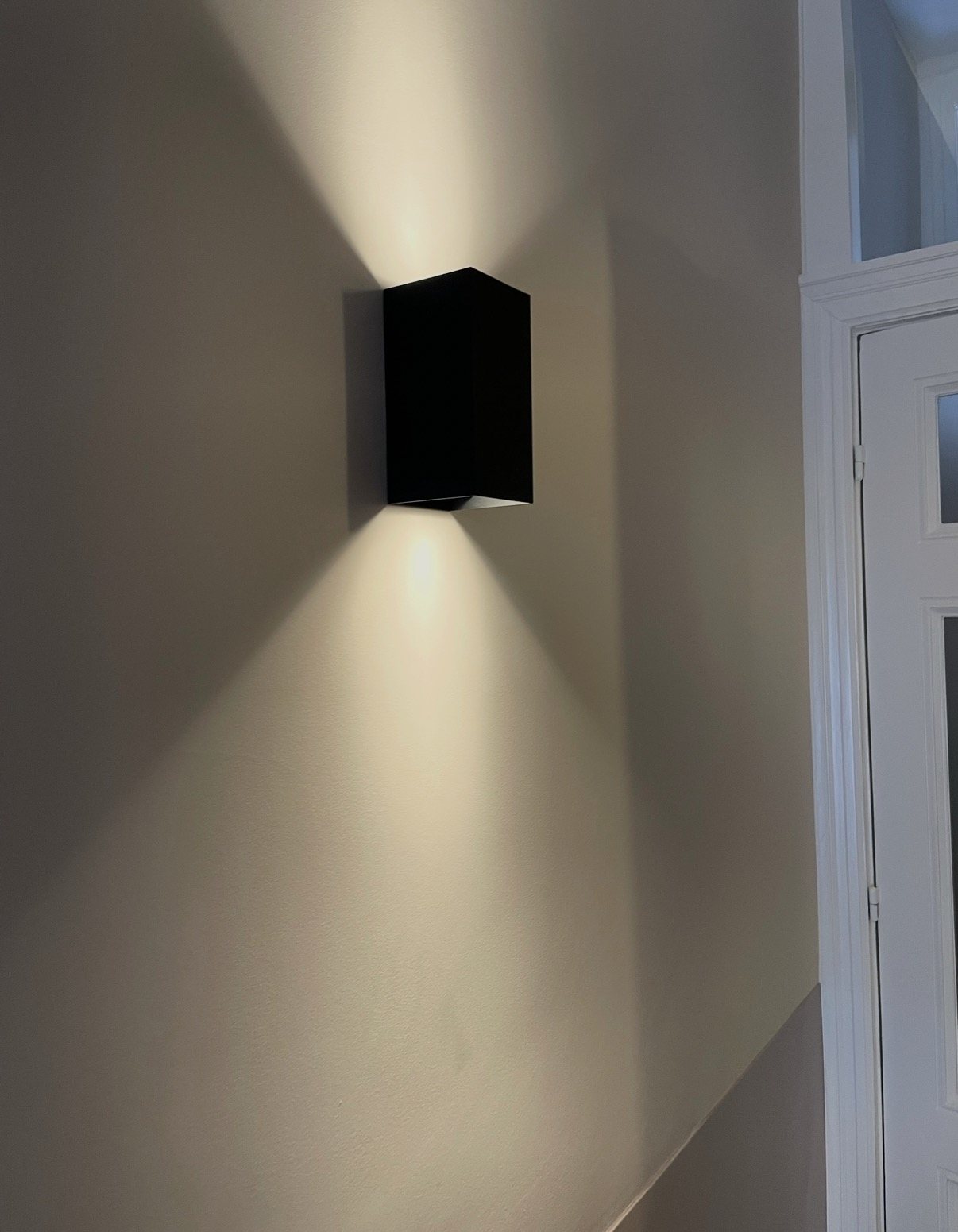 Zwarte wandlamp die licht naar boven en naar beneden geeft, in een trappenhuis.